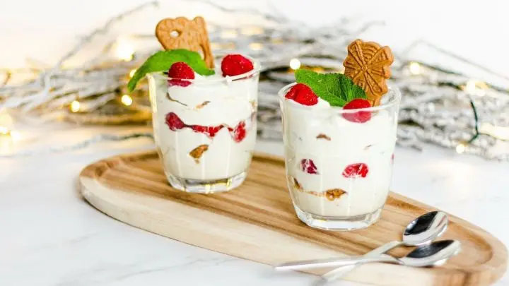 Zwei Gl&auml;ser mit Last Minute Spekulatius-Dessert sind auf einem Holzbrett angerichtet, garniert mit Himbeeren und Minze.