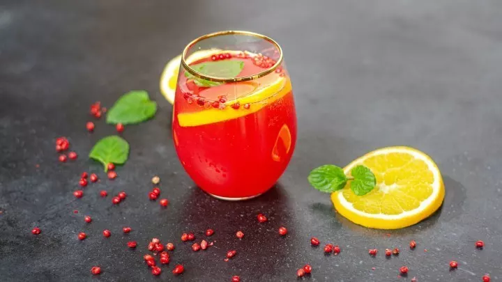 Ein bunt dekorierter Cocktail mit Cranberrys und Zitronenscheiben steht auf einer dunklen Oberfläche.