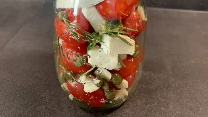 Schichte die Tomaten, die Fetawürfel und je Schicht dazu 1 Teelöffel Kapern und auch die Kräuter abwechselnd in das Glas und gib über jede Tomatenschicht 1 Prise Salz.