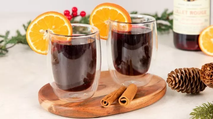 Zwei Gläser mit Lillet Hot Berry, gefüllt mit dunklem Getränk, serviert auf einem Holzbrett mit Orangen und Zimtstangen.