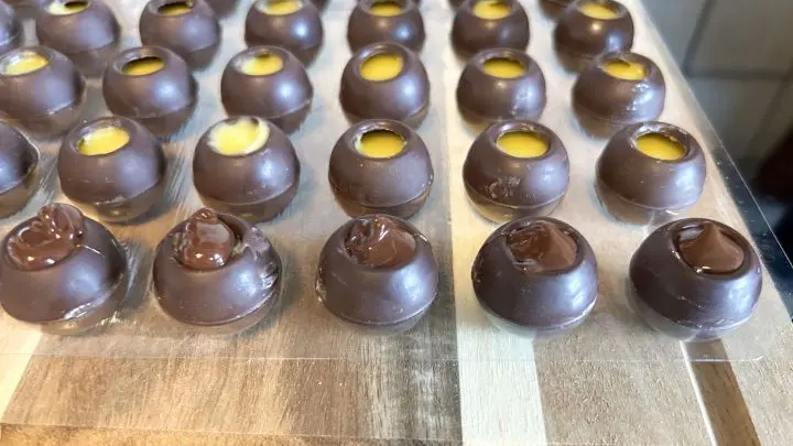 Die Pralinen werden nun mit Kuvertüre verschlossen. Gib dafür mit einem Teelöffel oder einem Spritztütchen etwas Schokolade auf die Öffnung. Danach mit einem Buttermesser glattstreichen.