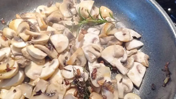 Die Zwiebelwürfel und die Knoblauchzehe sowie die Pilze werden in einer Pfanne angebraten und die Kräuter kommen ebenfalls dazu. 