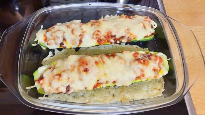 Die gef&uuml;llten, mit K&auml;se &uuml;berbackenen Zucchinih&auml;lften verlassen soeben den Backofen &ndash; man sieht die leckere K&auml;sekruste.