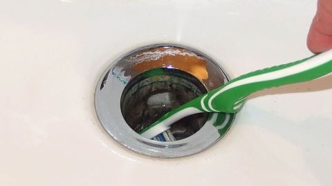 Mit einer alten Zahnbürste Haare aus dem Abfluss entfernen.