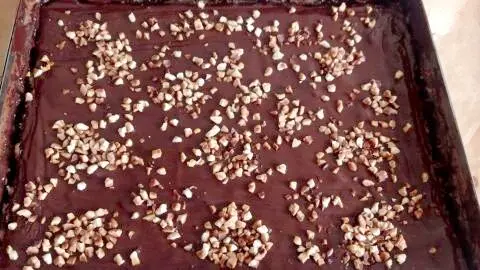 Nachdem alle weiteren Schichten gebacken sind, wird die geschmolzene Kuvertüre über dem Baumkuchen verteilt. Baumkuchen einfach vom Blech: Schokoladenguss und Nussdeko machen dieses Rezept zum Highlight auf jeder Kaffeetafel.