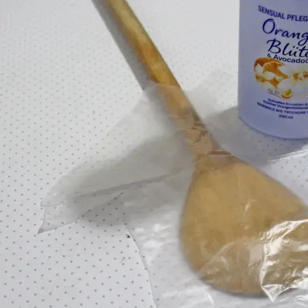 Rücken selbst eincremen mit Holzkelle und Einweghandschuh