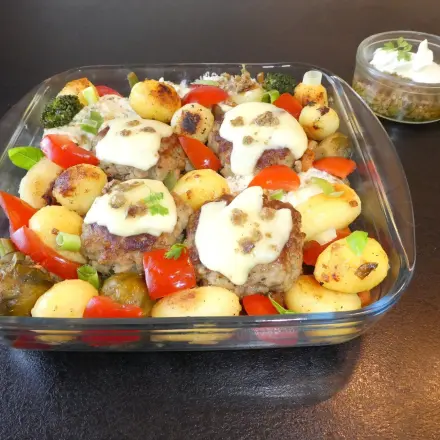 Mit Käse überbackene Pesto-Frikadellen im Gemüsebett