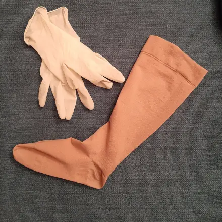Kompressionsstrumpf mithilfe von Einmalhandschuhen anziehen