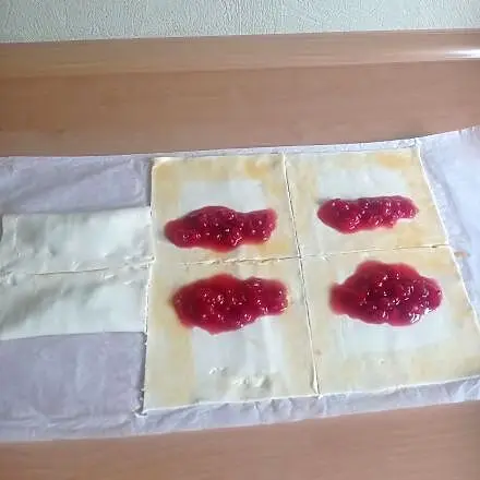 Aus dem Blätterteig schneidet man sechs gleich große Quadrate und belegt sie mit je einem TL der Johannisbeeren.